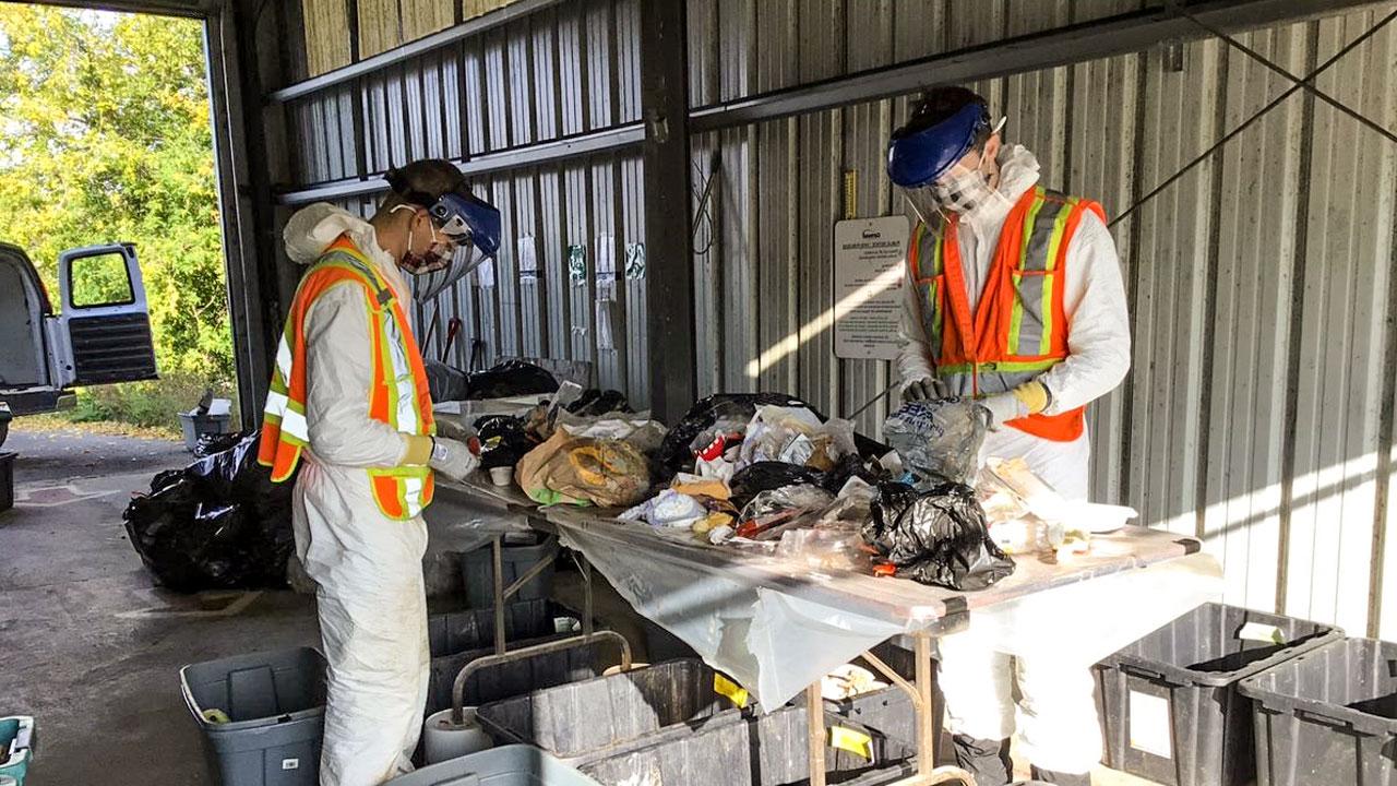 Two workers wearing PPE determining quantity of organic materials in waste stream