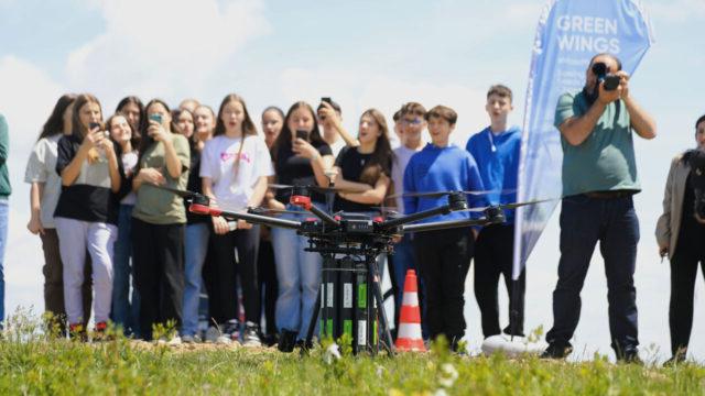 A group of youth standing in a field watch a drone prepare to take off