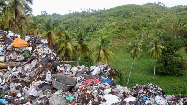 Open dump site with large pile of waste and plastic pollution next to an ecologically significant landscape